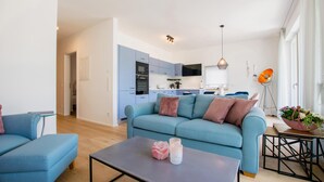 A modern living room with a blue sofa, a coffee table with decorative items, and a kitchen in the background. - Beary - modern ground floor flat in best location (Garmisch-Partenkirchen)