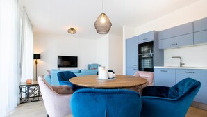 A modern kitchen with a dining area, featuring a round wooden table, blue chairs, and a TV in the background. - Beary - modern ground floor flat in best location (Garmisch-Partenkirchen)