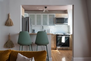 A modern kitchen with white cabinets, a microwave, and a stove. There are two green chairs in the foreground.