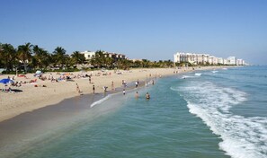 A beach with people, palm trees, and buildings in the background. - 1 Bedroom Garden Condo—Steps from the Beach (Pompano Beach)
