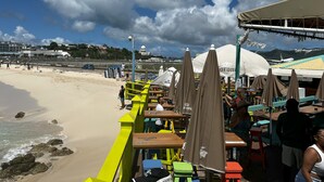 A beachside restaurant with outdoor seating, a view of the beach, and a distant view of a dome and airport.
