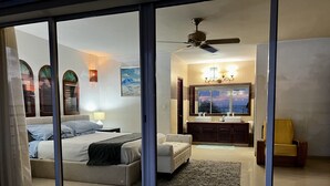 A modern bedroom with a large bed, a sofa, a bathroom with a vanity, and a view of the ocean.