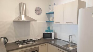 A modern kitchen with a gas stove, stainless steel range hood, white cabinets, a microwave, and a sink. - Mami "Holiday House" (Castellammare del Golfo)