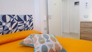 A bedroom with a bed, a nightstand, a wooden dresser, a door, and a wall with a geometric-patterned artwork. - Mami "Holiday House" (Castellammare del Golfo)