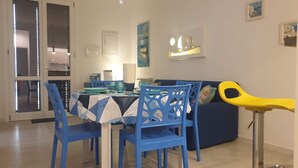 A dining area with a table set for two, blue chairs, a blue sofa, and a yellow chair. - Mami "Holiday House" (Castellammare del Golfo)