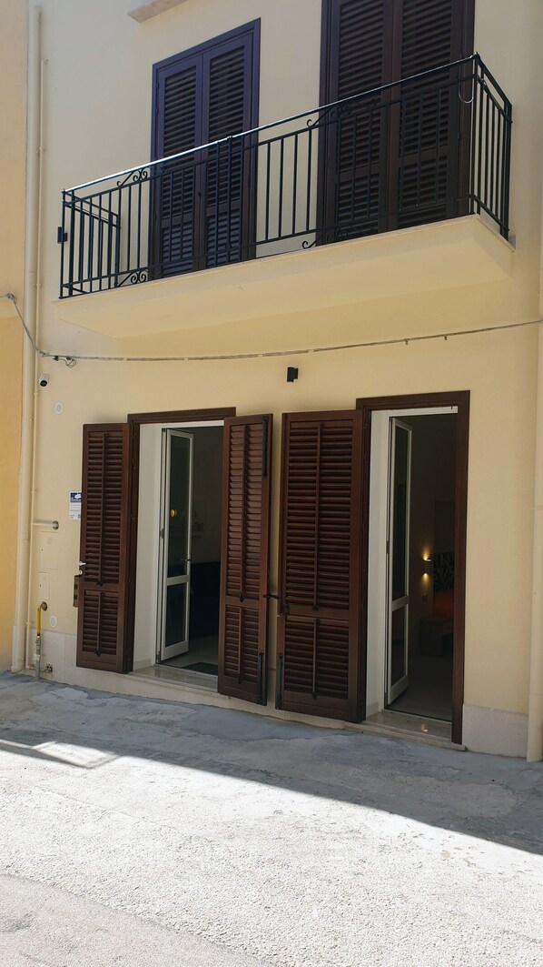 A two-story building with a balcony, wooden shutters, and a door.