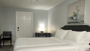Une chambre à coucher avec un lit, une table de chevet, une chaise et un tableau accroché au mur.