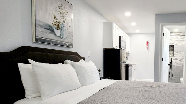 Une chambre d’hôtel avec un grand lit, un tableau au-dessus du lit, une kitchenette et une salle de bain visible par une porte ouverte.