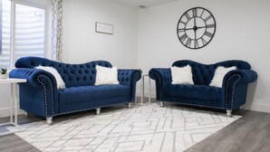 A room with two blue upholstered sofas with white pillows, a white rug, a wall clock, and a small table with a plant. - Modern 3-bedroom Guest Suite by Silicon Slopes (Eagle Mountain)