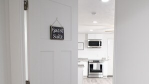 A white door with a sign reading "Guest Suite" and a view into a modern kitchen with white cabinets and stainless steel appliances. - Modern 3-bedroom Guest Suite by Silicon Slopes (Eagle Mountain)