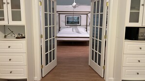 A bedroom with a bed, a ceiling fan, and a TV. There are two white cabinets with glass doors on either side of the bed. - Beach House in waterfront gated community w/ salt water pool (Lewes)