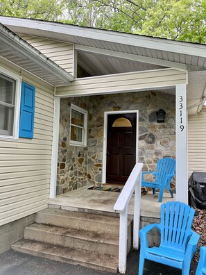 A house with a stone facade, a dark brown door, and the number 3319 on the wall. There are two blue chairs outside.