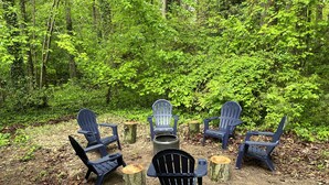 A forest clearing with five Adirondack chairs arranged around a central fire pit. - Beach House in waterfront gated community w/ salt water pool (Lewes)