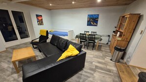 A living room with a black sofa, a wooden table, and a dining area with chairs and a table. - Pleasant 1 Bedroom Villa with Private Pool / Yard (Vensac)