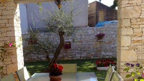 Eine Terrasse im Freien mit einer Steinmauer, einem Tisch mit Stühlen und einem Blumentopf mit einem Baum.