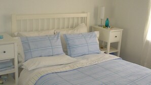 Ein Schlafzimmer mit einem Bett, zwei Nachttischen, einem gerahmten Bild an der Wand und einem Fenster mit Vorhängen.