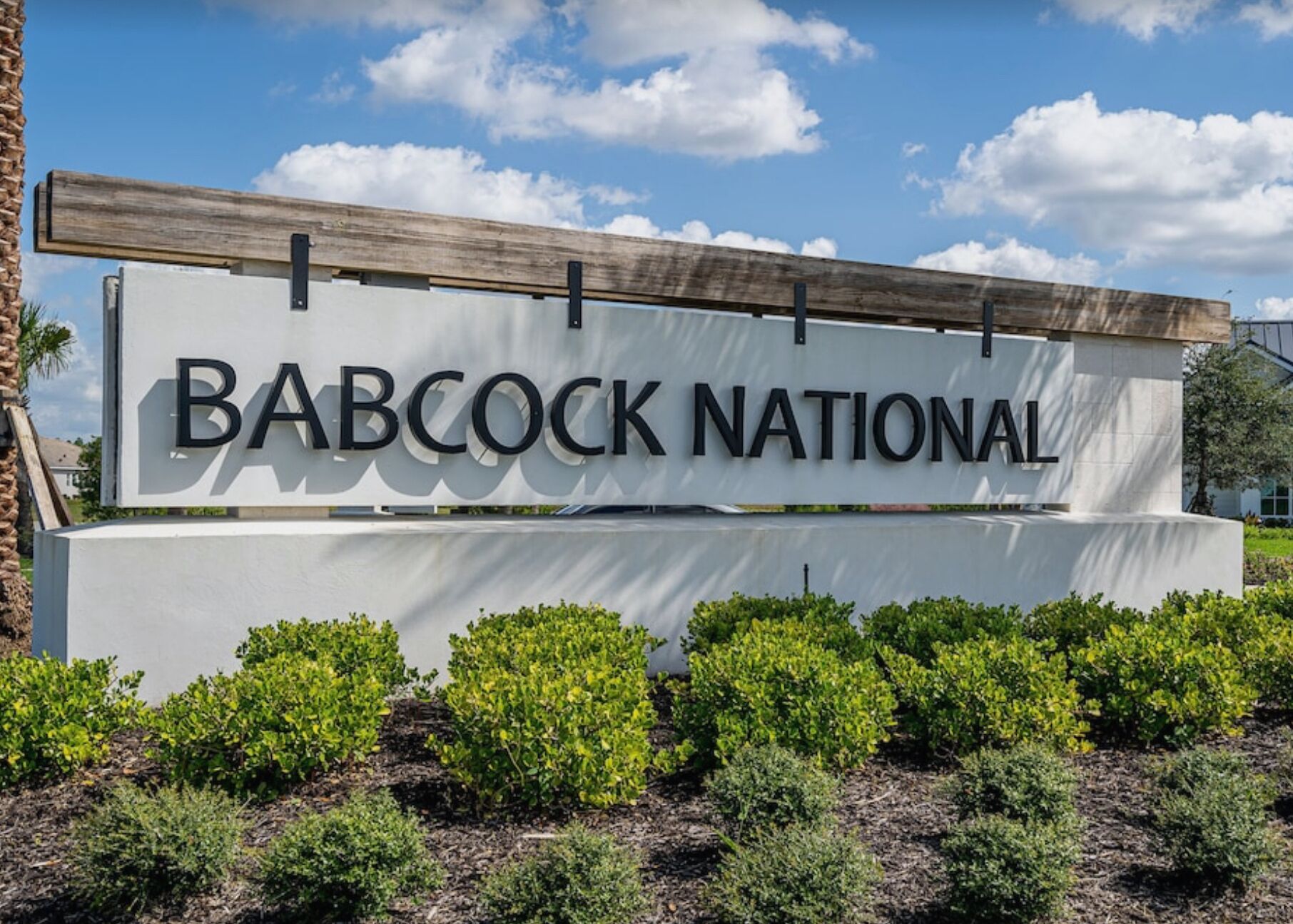 A sign for Babcock National with a wooden beam above it and green shrubs in front.
