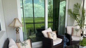 Una habitación iluminada por el sol con muebles de mimbre, un ventanal de vidrio que da a un césped verde y una planta en maceta.