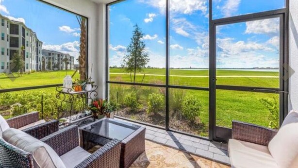 Un balcón con mobiliario de mimbre, una mesa de vidrio y vistas a un campo verde y edificios.