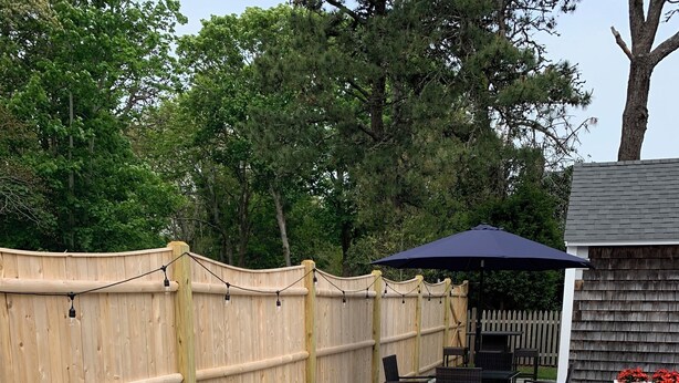 Une terrasse extérieure avec une clôture en bois, une table avec des chaises et un barbecue.