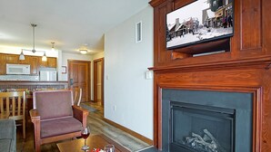 Ein gemütliches Wohnzimmer mit Kamin, ein Essbereich mit Tisch für zwei Personen und eine Küche im Hintergrund.