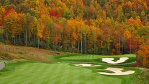 Ein Golfplatz mit einem gepflegten Grün, Sandbunkern und einem Hintergrund aus herbstlich gefärbten Bäumen.