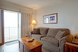 Relax in this inviting living area with a sofa, coffee table, and framed artwork, leading out to a balcony.