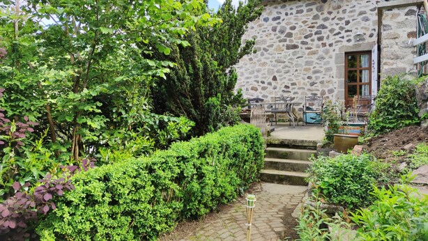 A stone house with a garden path leading to a patio area with outdoor furniture.
