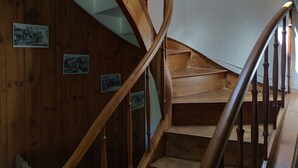 A wooden spiral staircase with a white wall and pictures on the wall.