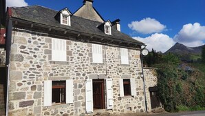 A stone building with a gabled roof, multiple windows with shutters, and a small porch area.