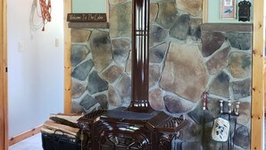 A wood-burning stove in a cabin with a stone wall and wooden ceiling.