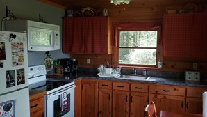 A compact kitchen with wooden cabinets, a microwave, a stove, a sink, and a window with a view of the outdoors.