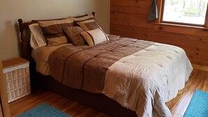 A wooden-paneled room with a bed, a wicker basket, and a window with curtains.