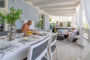 Ein Essbereich im Freien mit einem Tisch, der für eine Mahlzeit gedeckt ist, umgeben von Stühlen und einem überdachten Sitzbereich.