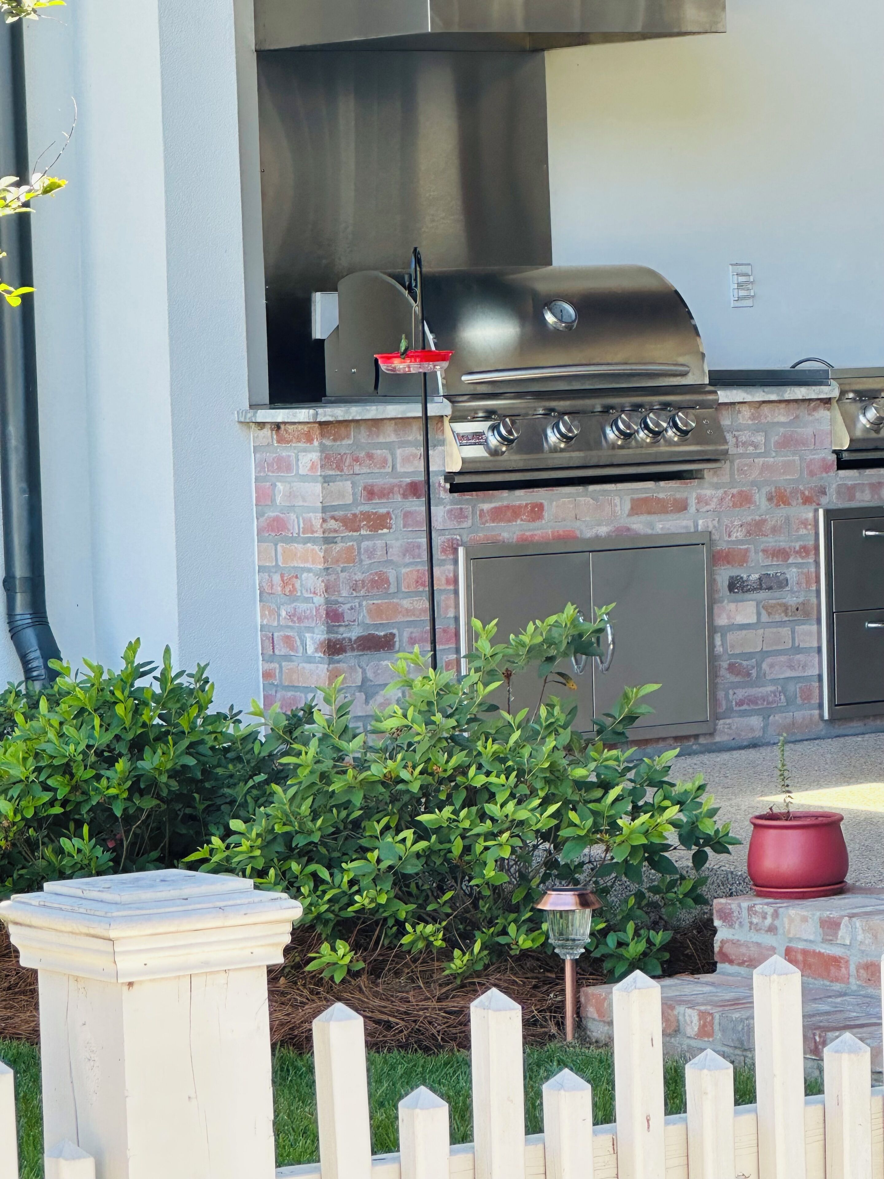 Cocina exterior con una parrilla de acero inoxidable, paredes de ladrillo y cerca de madera.