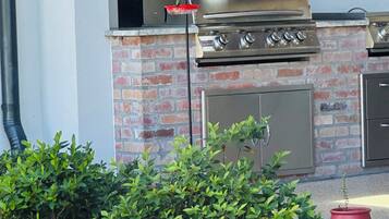 Cocina exterior con una parrilla de acero inoxidable, paredes de ladrillo y cerca de madera.