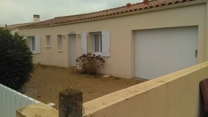 Un edificio con techo de tejas, varios portones de garaje y un pequeño jardín con un arbusto.