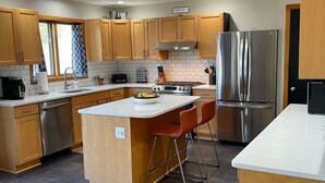 A modern kitchen with wooden cabinets, stainless steel appliances, a central island with stools, and a "Good Day" sign. - Welcoming retreat close to Cornell, Ithaca College, and Cayuga Lake (Ithaca)