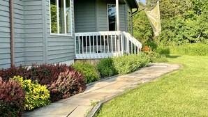 A house with a front porch, a pathway leading to the entrance, and a garden with various plants and flowers. - Welcoming retreat close to Cornell, Ithaca College, and Cayuga Lake (Ithaca)