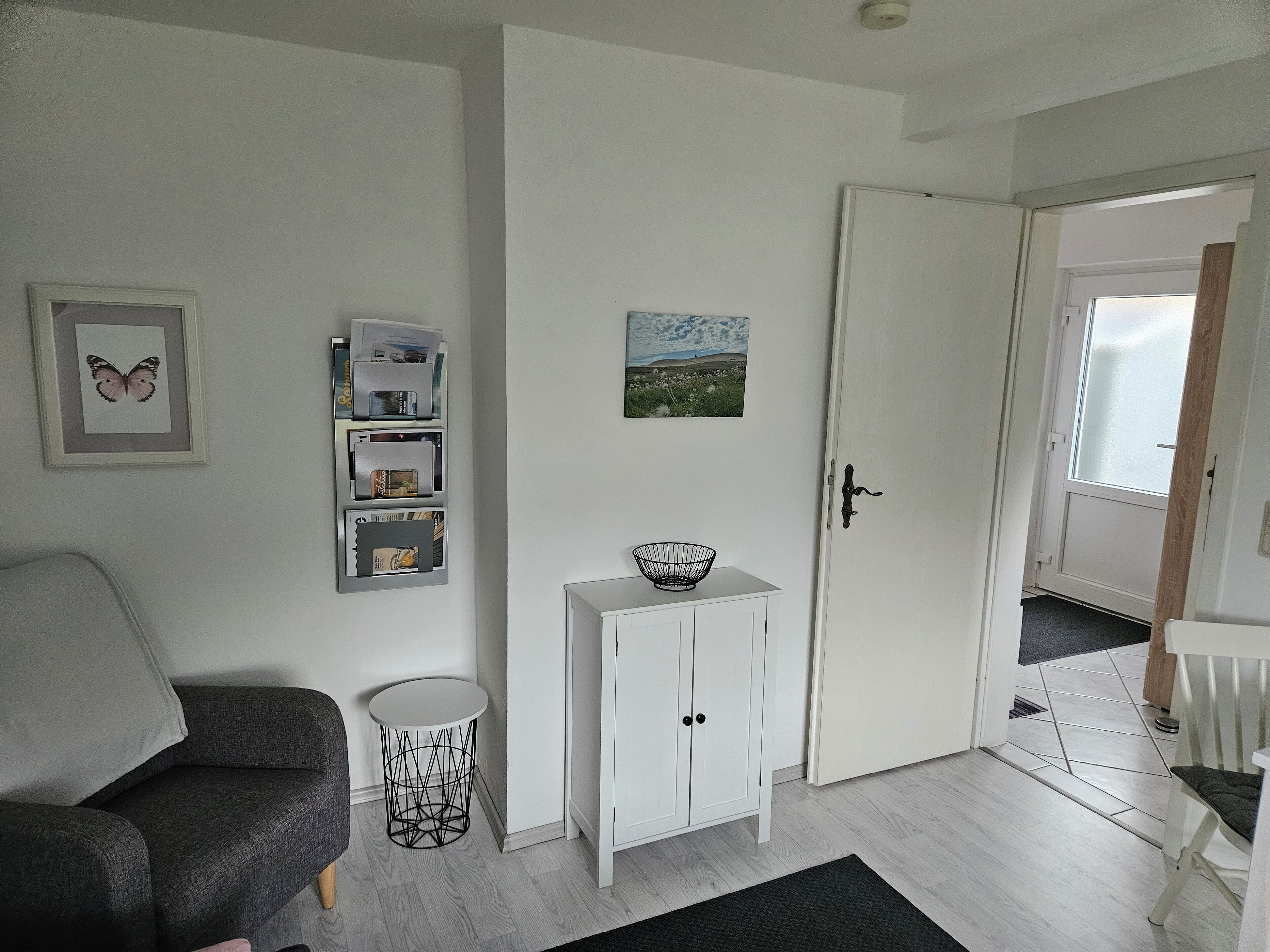 A modern living room with a grey sofa, a white cabinet, a small round table, and a door leading to another room.