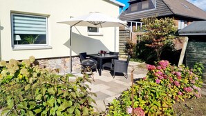 Eine Terrasse mit Tisch und Stühlen, einem Grill und einem großen Sonnenschirm.