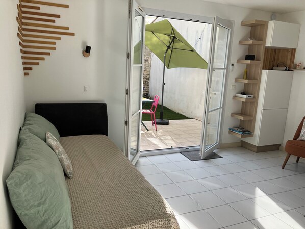 A room with a bed, a green umbrella, a pink chair, and a white tiled floor.