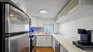 A modern kitchen with stainless steel appliances, white cabinets, a tiled backsplash, and a coffee maker. - Fort Lauderdale House (Fort Lauderdale)
