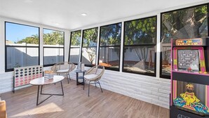 A bright room with large windows, a small table, two wicker chairs, and a retro arcade machine. - Fort Lauderdale House (Fort Lauderdale)