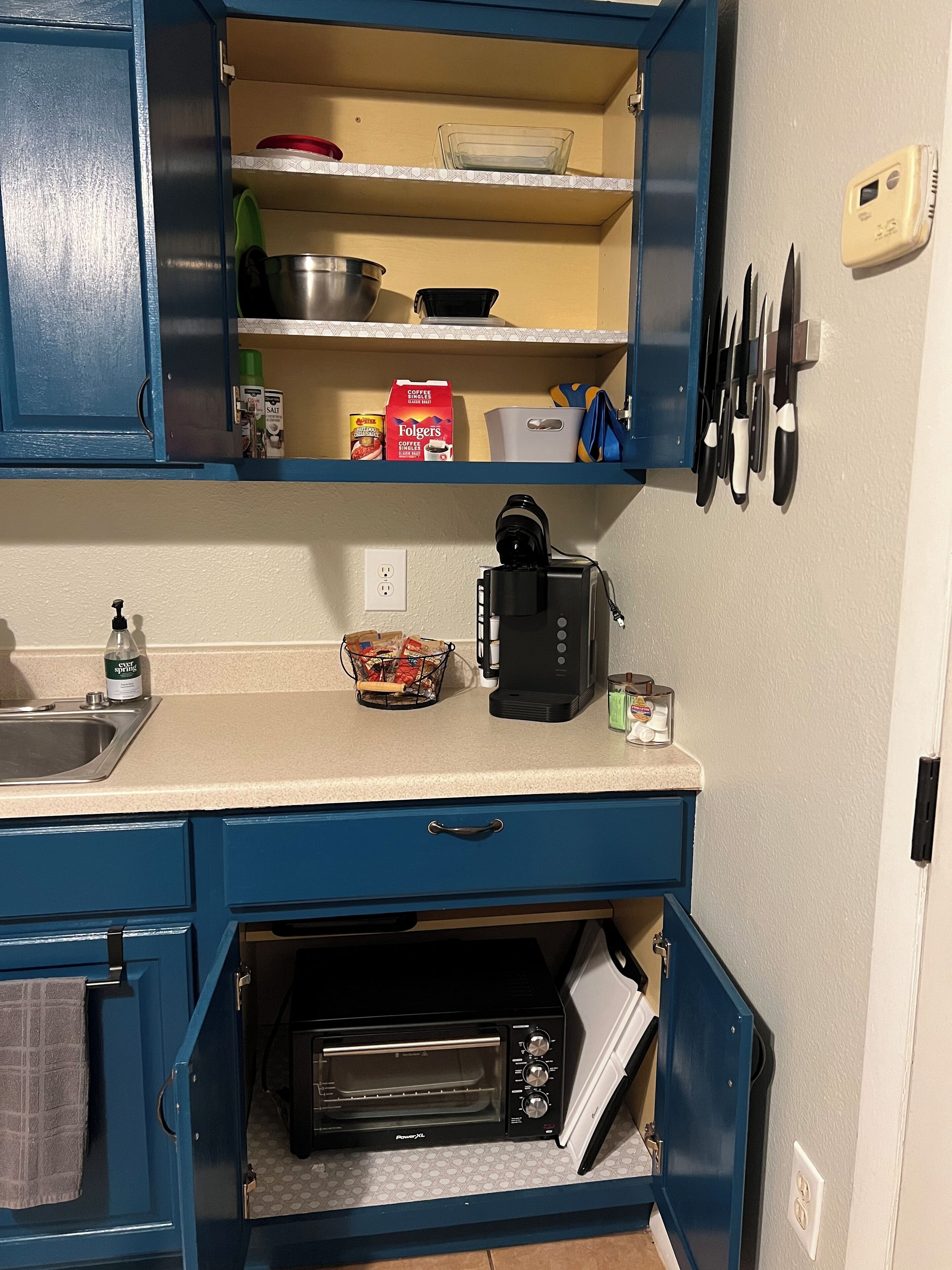 A compact kitchen with a toaster oven, coffee maker, and a shelf with kitchenware.