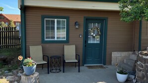 A single-story house with a green door, two windows, and a porch with two chairs and a table. - Mil Suite-1-bedroom cottage with surrounding mountain views (La Veta)
