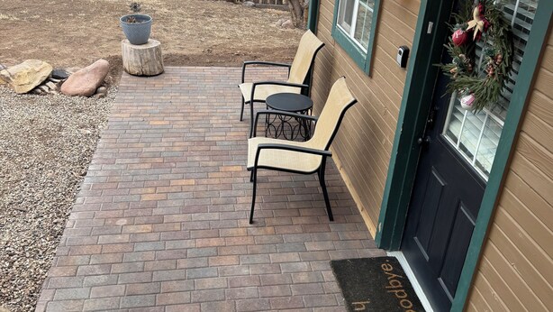 A brick patio with two chairs and a small table, a wooden fence, and a door with a wreath. - Mil Suite-1-bedroom cottage with surrounding mountain views (La Veta)