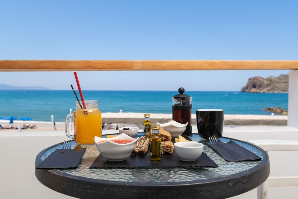 A table with a meal setup overlooking the sea, including a drink, bread, and condiments.