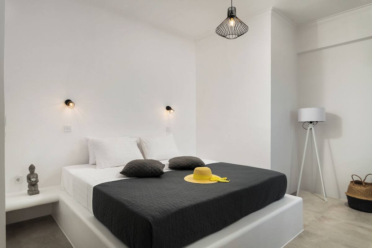 A modern bedroom with a bed, bedside lamps, a floor lamp, and a small statue.