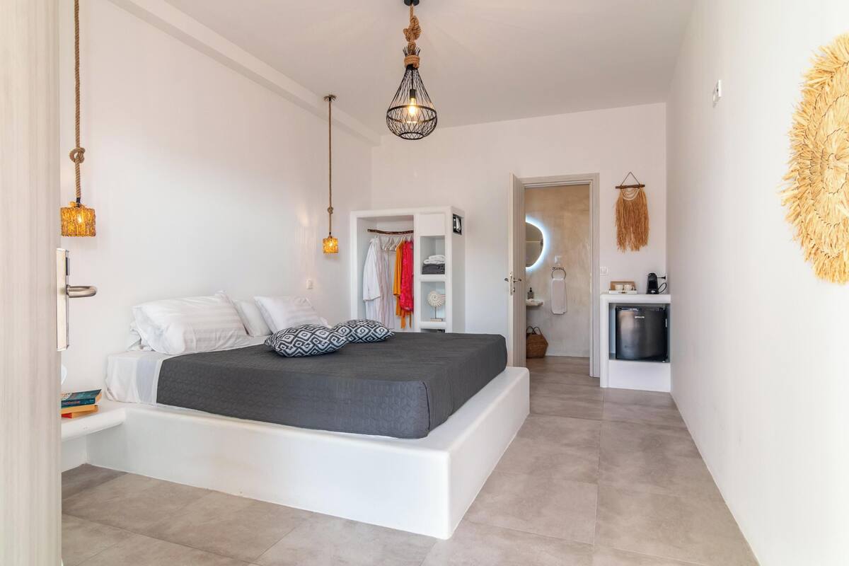 A modern bedroom with a large bed, bedside tables, a wardrobe, and a bathroom visible through an open door.
